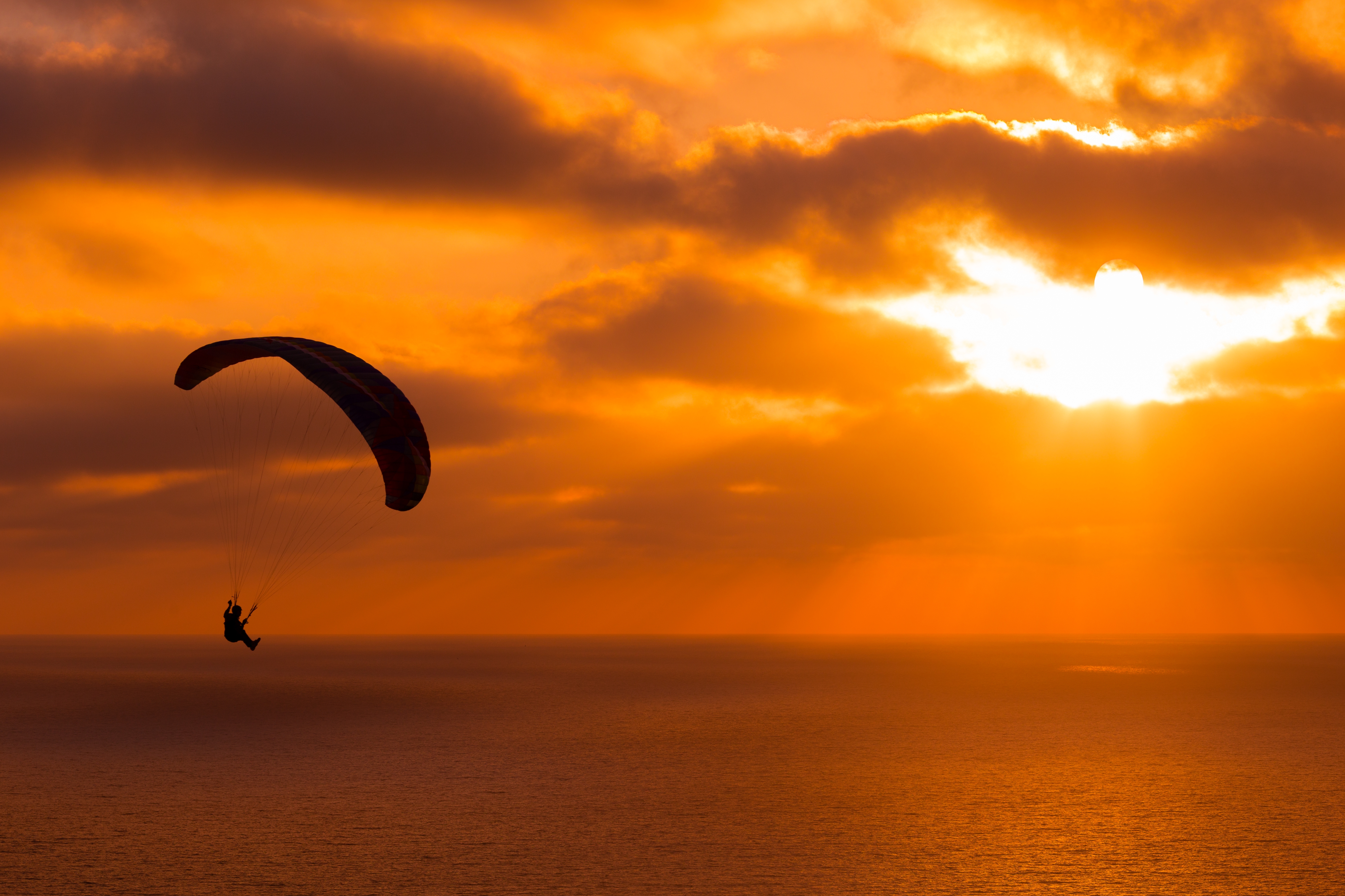 un parapente dans la lumière du soleil couchant planant au dessus de la mer.